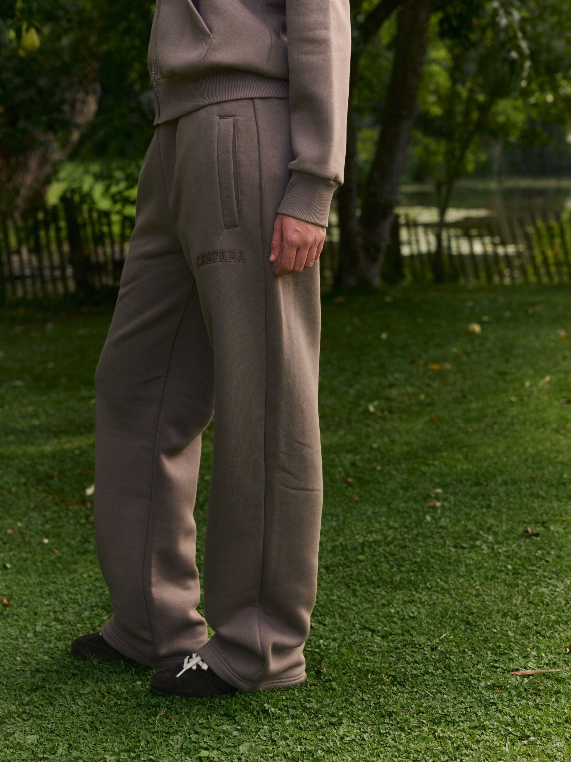 Woman wearing walnut straight-leg sweatpants standing outdoors on a green lawn.